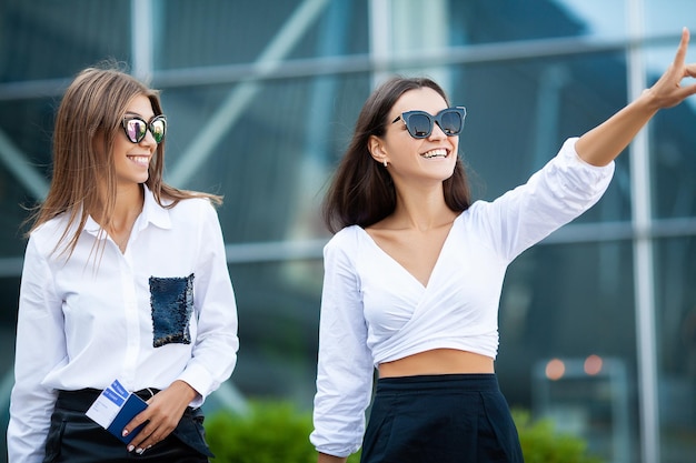 Two stylish female travelers walking with their luggage in airport