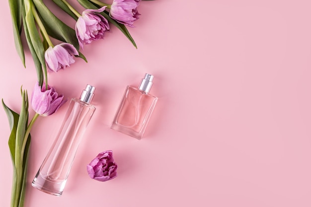 Two stylish glass bottles with perfume on a pink background among spring flowers A copy space Top view Perfume and beauty concept