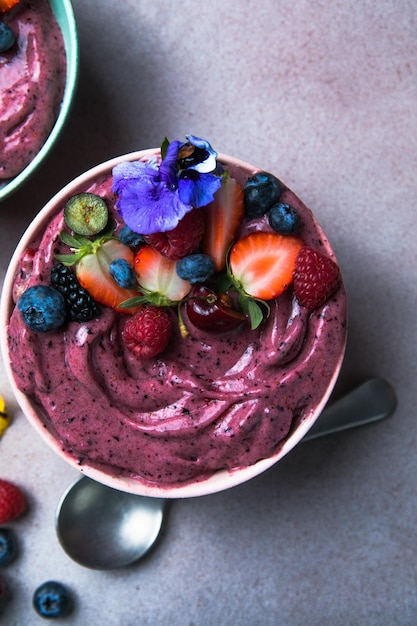 Two summer acai smoothie bowls with strawberries blueberries on gray concrete background Breakfast bowl with fruit and cereal closeup top view healthy food