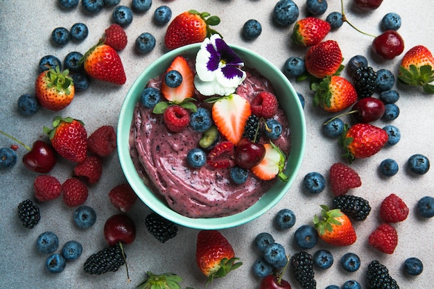 Two summer acai smoothie bowls with strawberries blueberries on gray concrete background Breakfast bowl with fruit and cereal closeup top view healthy food