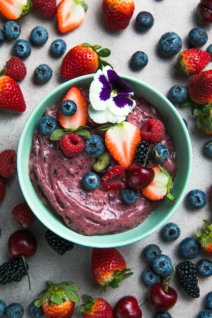 Two summer acai smoothie bowls with strawberries blueberries on gray concrete background Breakfast bowl with fruit and cereal closeup top view healthy food