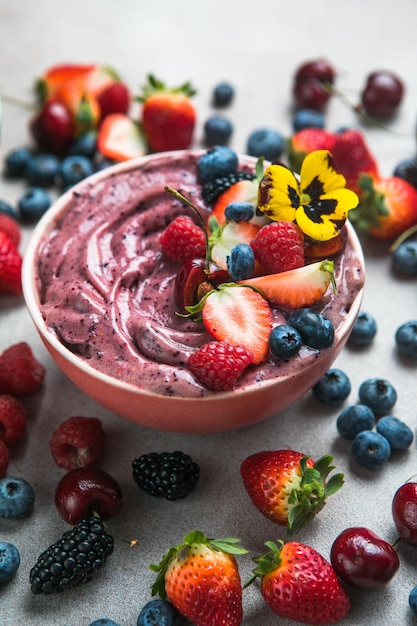 Two summer acai smoothie bowls with strawberries blueberries on gray concrete background Breakfast bowl with fruit and cereal closeup top view healthy food