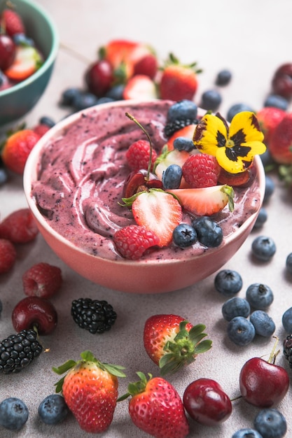 Two summer acai smoothie bowls with strawberries blueberries on gray concrete background Breakfast bowl with fruit and cereal closeup top view healthy food