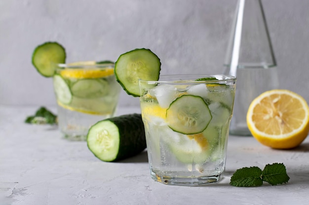 Two summer fresh ice drinks with mint lemon and cucumber plus a bottle of mineral water Healthy mojito detox cocktail on gray background