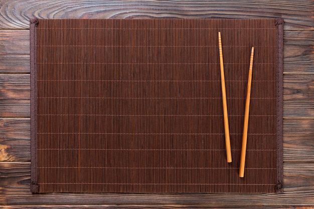 Two sushi chopsticks with empty bamboo mat or wood plate on wooden Background