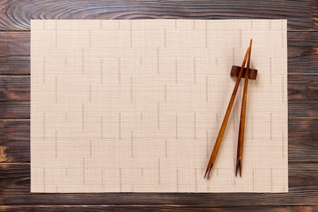 Two sushi chopsticks with empty brown bamboo mat or wood plate on wood