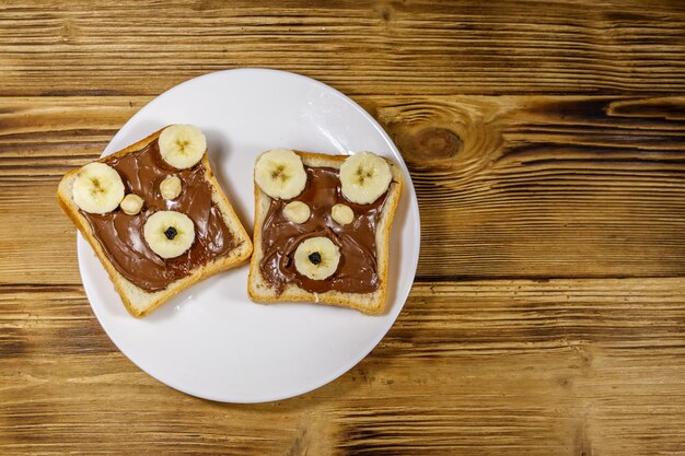 Two sweet sandwiches with delicious chocolate hazelnut spread and banana in shape of bear on wooden table Top view