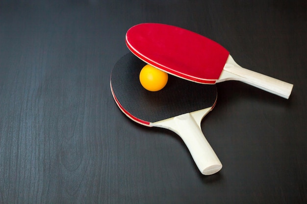 Two table tennis or ping pong rackets and ball on a black background