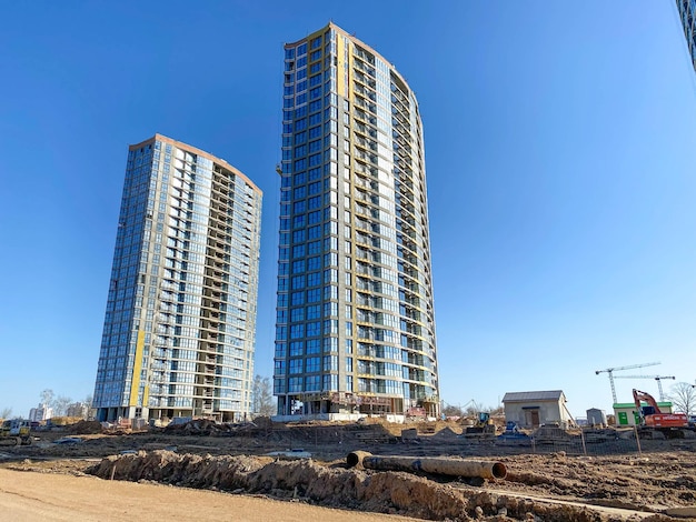 Two tall beautiful modern unfinished new buildings made of glass and concrete against a blue sky