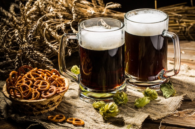 Two tankard beer with wheat and hops , basket of pretzels