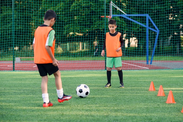 Two teen players passes soccer ball each other on football stadium.