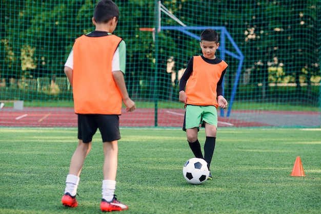 Two teen players passes soccer ball each other on football stadium.