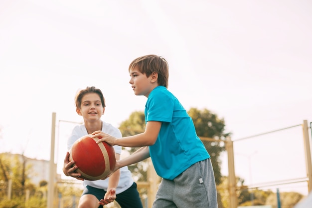 Two teenage boys play basketball on the Playground. Athletes fight for the ball in the game.