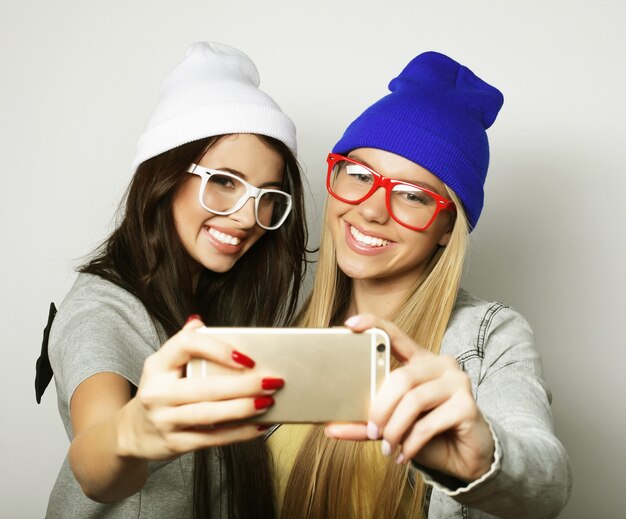 Two teenage girls friends in hipster outfit make selfie over white background