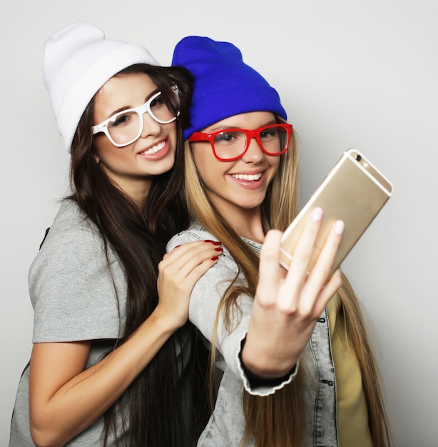 Two teenage girls friends in hipster outfit make selfie over white background