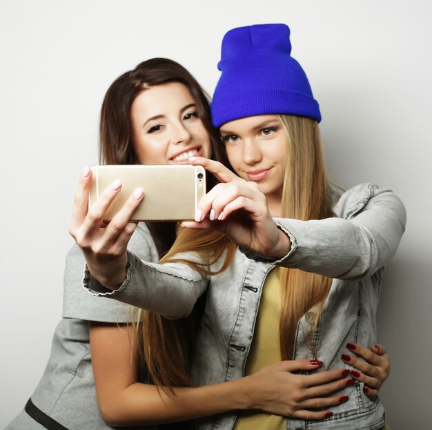 Two teenage girls friends in hipster outfit make selfie over white background