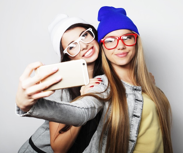 Two teenage girls friends in hipster outfit make selfie over white background