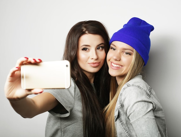 Two teenage girls friends in hipster outfit make selfie over white background