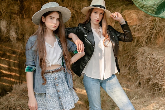 Two teenage girls posing in hayloft against background of stacks of hay