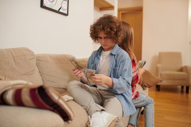 Two teens sitting on the sofa and holding dollars in hands