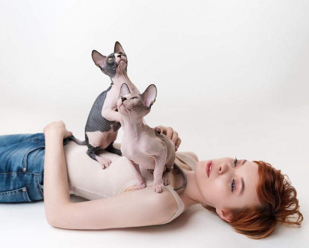 Two thoroughbred kittens looking up sitting on redhead young woman lying on back on white background