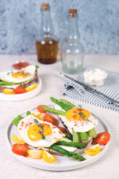 Two toasts with asparagus, ricotta and fried egg on black bread. Vertical photo, selective focus.