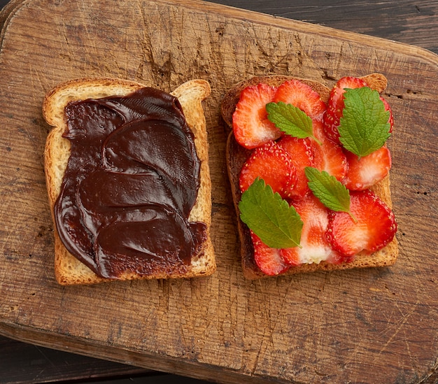 Photo two toasts with chocolate paste and fresh ripe red strawberries on a brown wooden board