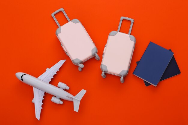 Two toy travel luggage, air plane and passport on orange. Travel planning