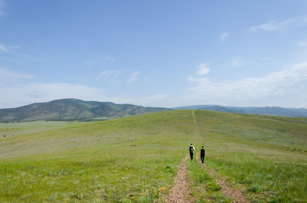 Two travelers walk along the road among the green hills Hiking in nature