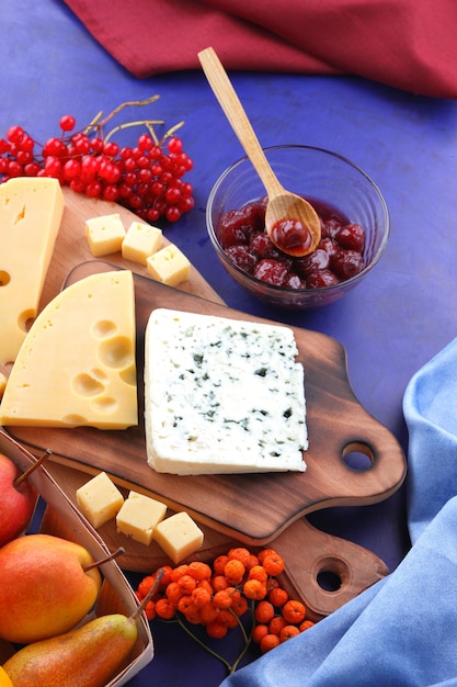 Two types of cheese on a wooden board with fruits and berries closeup Cheeses with honey on a blue background with blue and red napkins