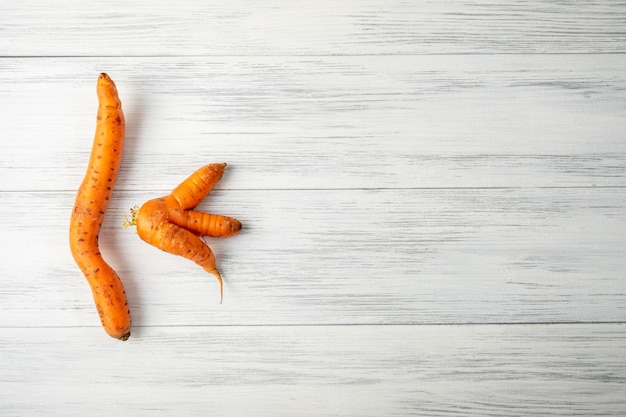 Two ugly carrots lie on a light wooden surface