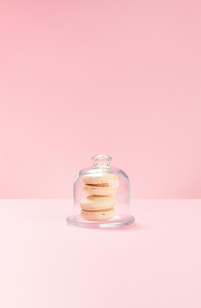 Two vanilla macarons lie in a candy jar on a pink background