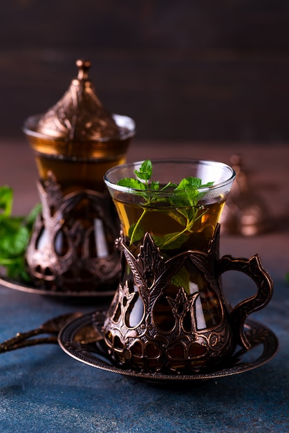 Two vintage glasses in the bronze cup holders with fresh tea and twig of green mint inside on a dark background.