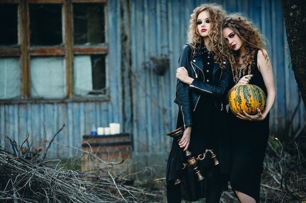 Two vintage women as witches, posing in front of an abandoned house on the eve of Halloween