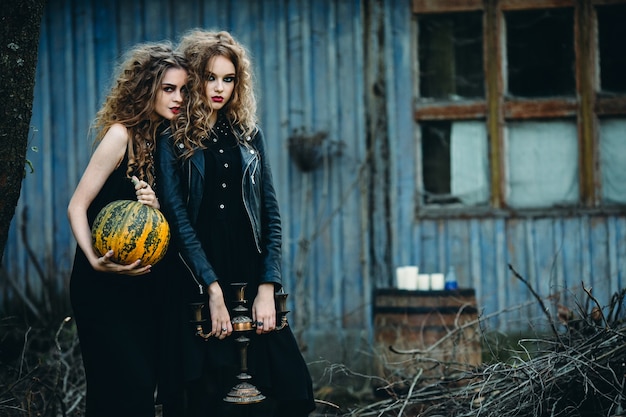 Two vintage women as witches, posing in front of an abandoned house on the eve of Halloween