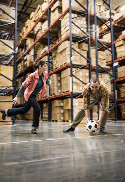 Two warehouse workers playing soccer during a work break in a distribution warehouse