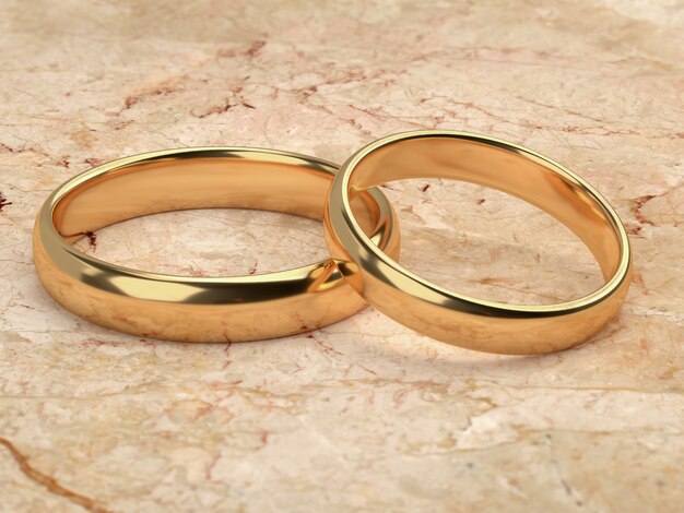 Two wedding gold rings lie next to each other on marble background