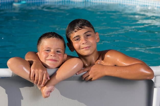 Two wet boys leaning on board the pool smiling on a background of blue water