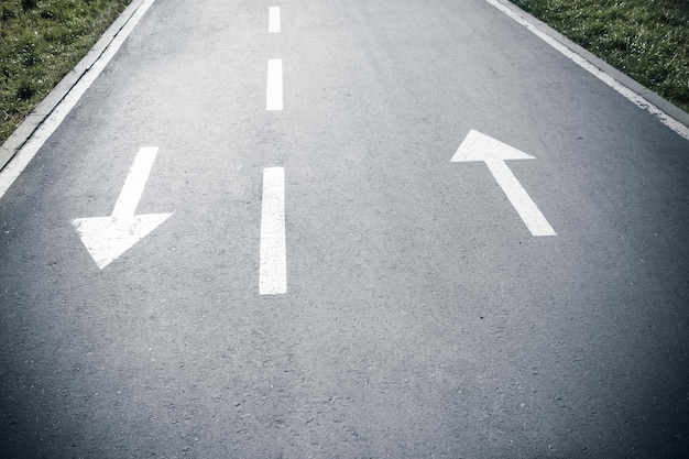 Photo two white arrow signs on opposite direction on asphalt road both sides sign up and down arrows direction for traffic safety way pointer on gray asphalt floor