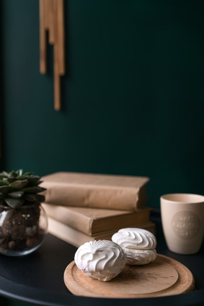 Two white beautiful delicious marshmallows lies on the table next to a cup of coffee and books on the table. High quality photo