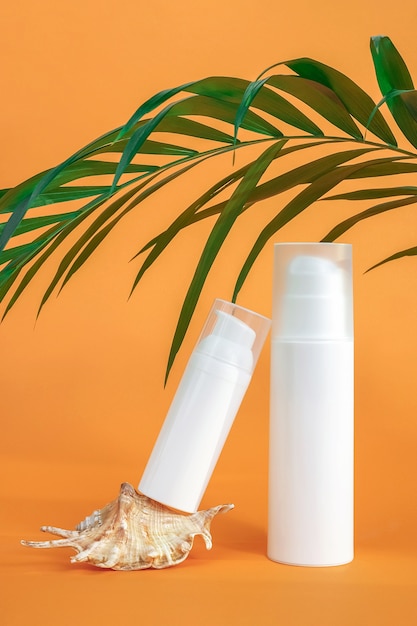 Two white blank cosmetics bottles with sunscreen, suncream or other cosmetic product, seashell and palm