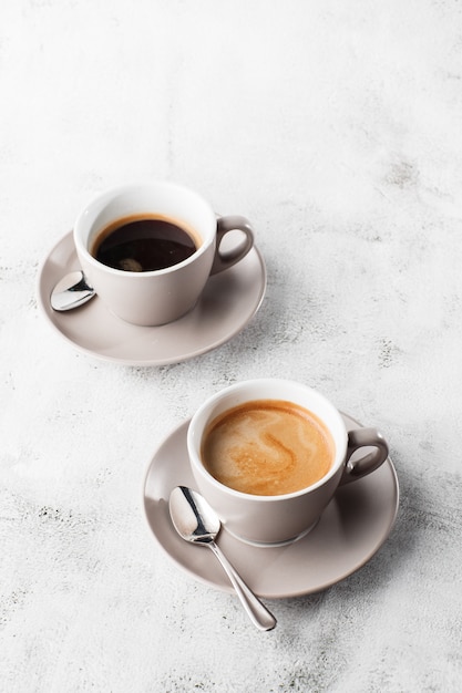 Two white cups of hot black coffee with milk isolated on bright marble background. Overhead view, copy space. Advertising for cafe menu. Coffee shop menu. Vertical photo.