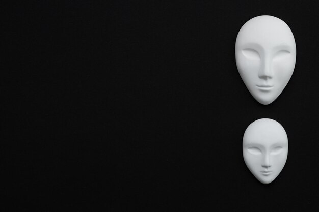 Photo two white gypsum mask of human with closed eyes on black background