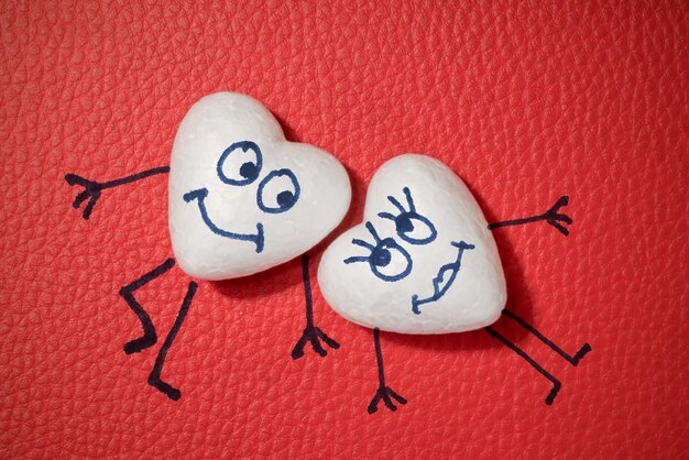 Two white hearts with happy faces on red leather background