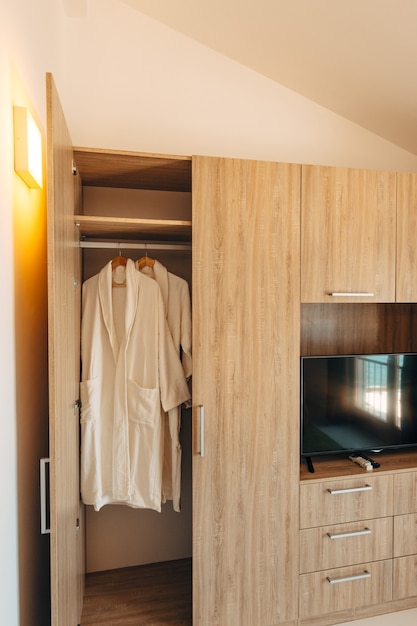 Two white robes inside a closet with an open door and a niche under a plasma TV