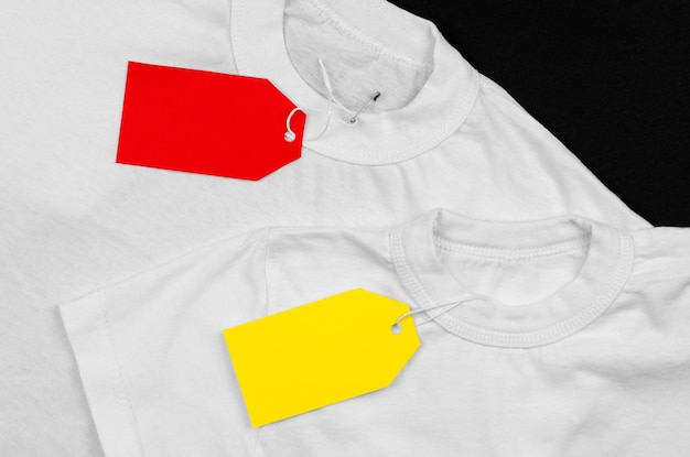 Photo two white t-shirts on a black background with empty price tags blank label on clothes