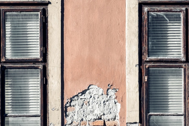 Two windows on the facade of an old house with peeling plaster