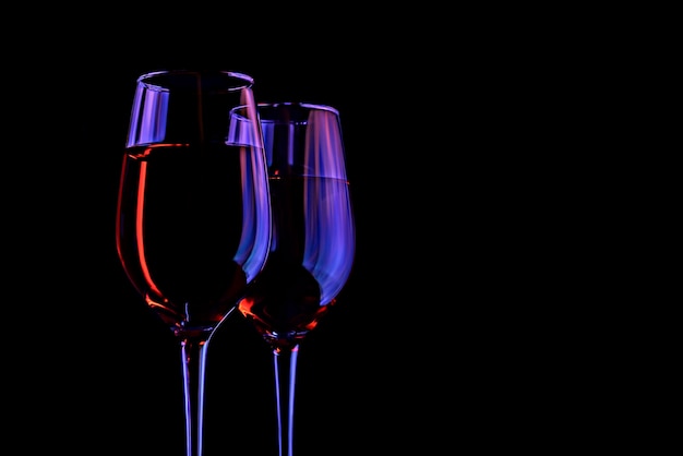 Two wine glasses on a dark background with neon highlights Creative party concept