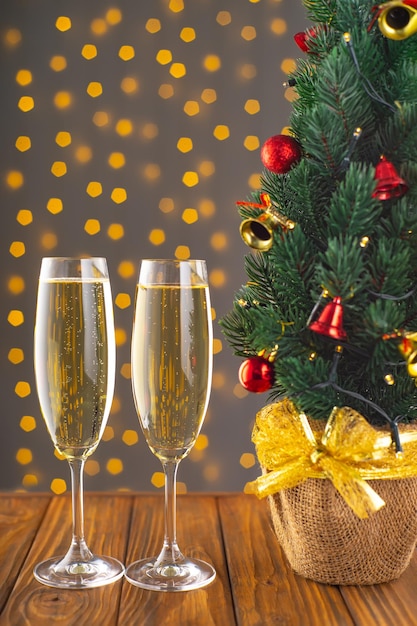 Two wine glasses with bubbly Champagne on blurry sparkling lights background and Christmas tree