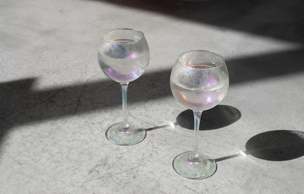 Two wine glasses with water on light concrete background with hard shadows